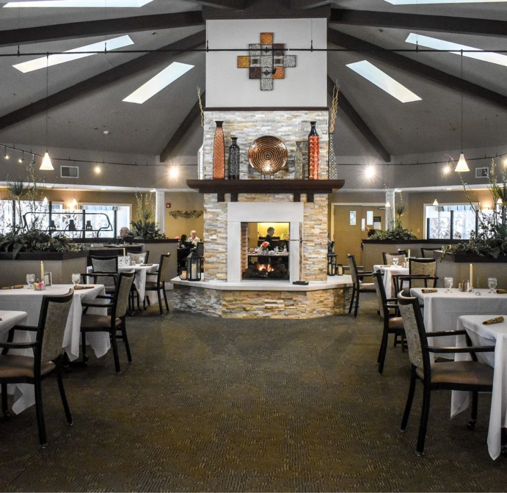 The Courtyard restaurant at Willow Brook Village in Delaware, Ohio, with vaulted beams and a central fireplace creating a formal dining atmosphere for senior residents.