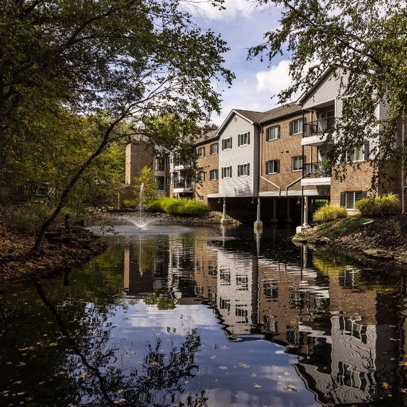 Tranquil pond with a fountain mirrors the multi-story Willow Brook Village residences in Delaware, Ohio — a defining view of this charming senior living community.